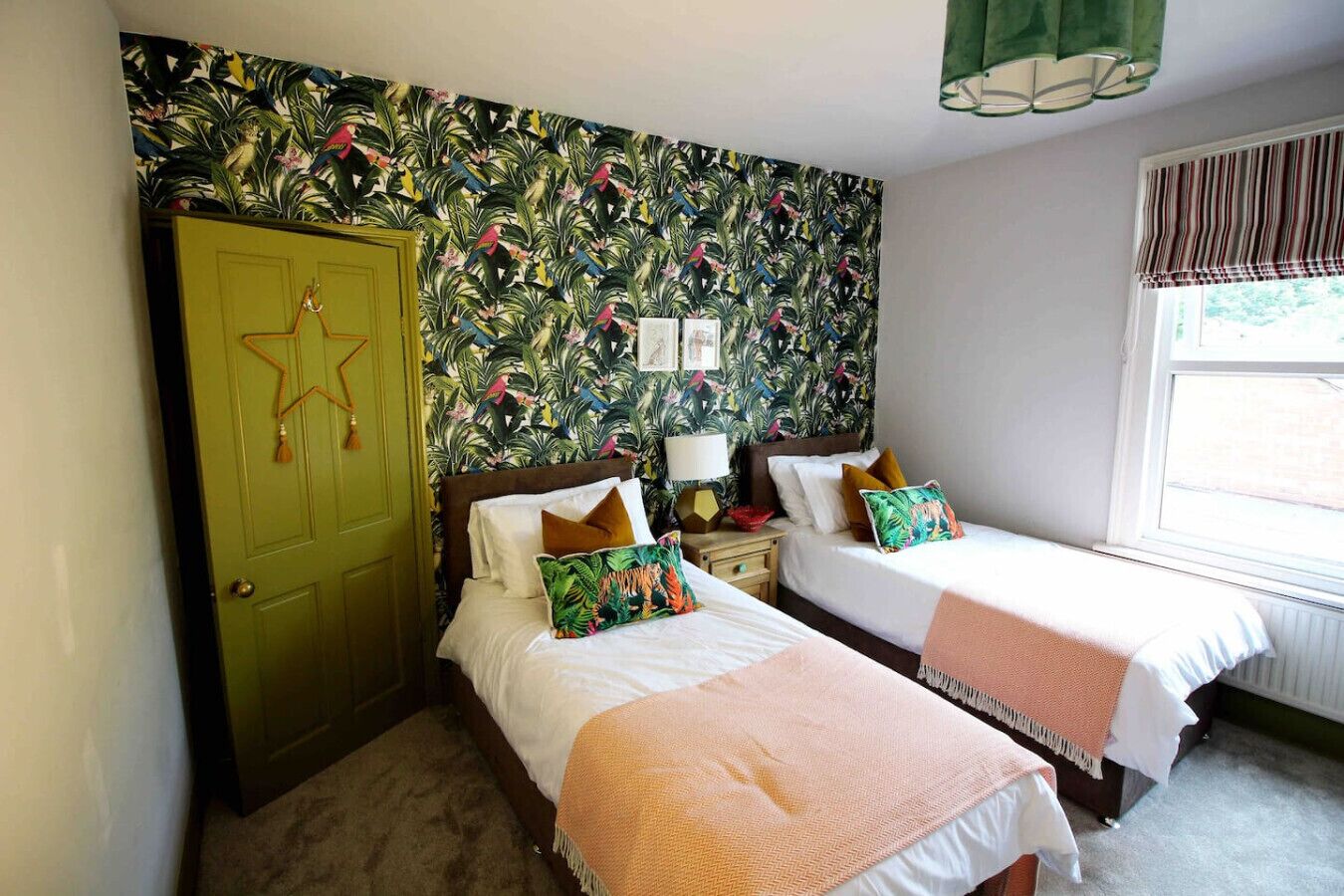 A room with two beds, a green door, and a tropical wallpaper.