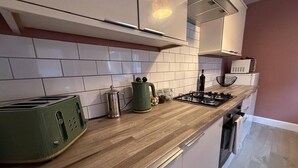 A kitchen with white cabinets, a wooden countertop, a green toaster, a kettle, a gas stove, and a microwave. - The Maple House common views, central Lincoln (Lincolnshire)