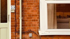 A brick house with a white door marked '23', a window with a curtain, and a visible light fixture. - The Maple House common views, central Lincoln (Lincolnshire)