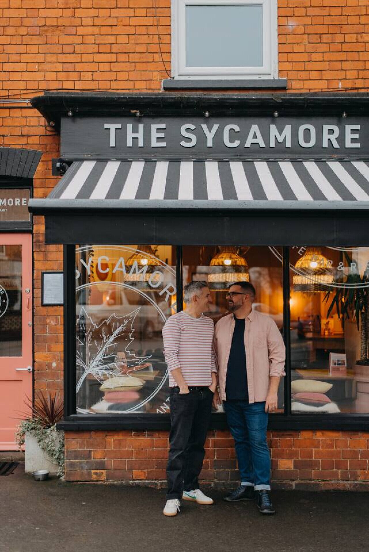 Fasaden på The Sycamore består av tegel, och byggnaden har ett svart- och vitrandigt markis och ett stort fönster där restaurangens namn visas.