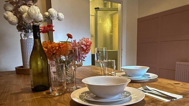 A dining table set with white plates, bowls, and cutlery, accompanied by a wine bottle and floral arrangements. - The Maple House common views, central Lincoln (Lincolnshire)