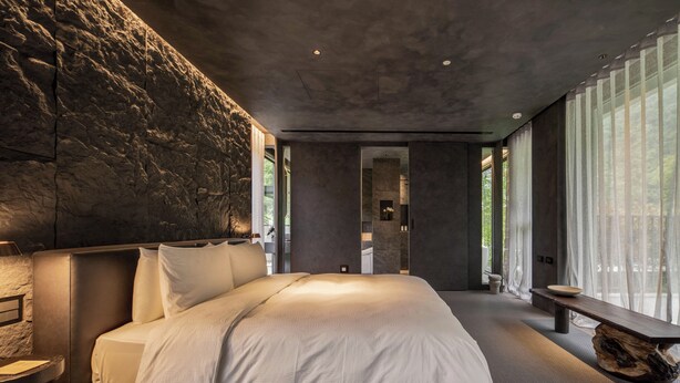 Ein modernes Schlafzimmer mit einem großen Bett, einer Steinwand und Blick auf ein Badezimmer.