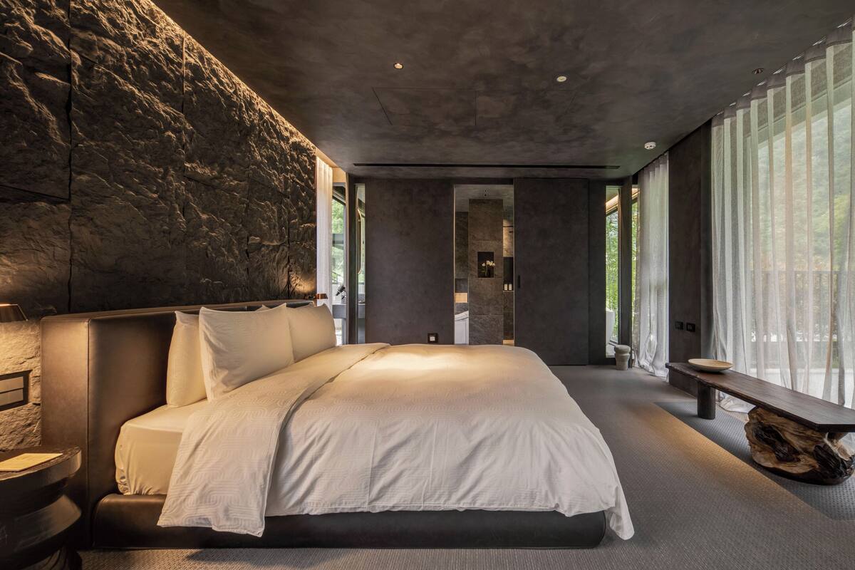 Een moderne slaapkamer met een groot bed, een stenen muur en uitzicht op een badkamer.