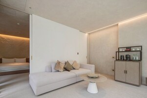 Una habitación de hotel moderna con sofá, una mesita de café y un armario con artículos de cortesía.