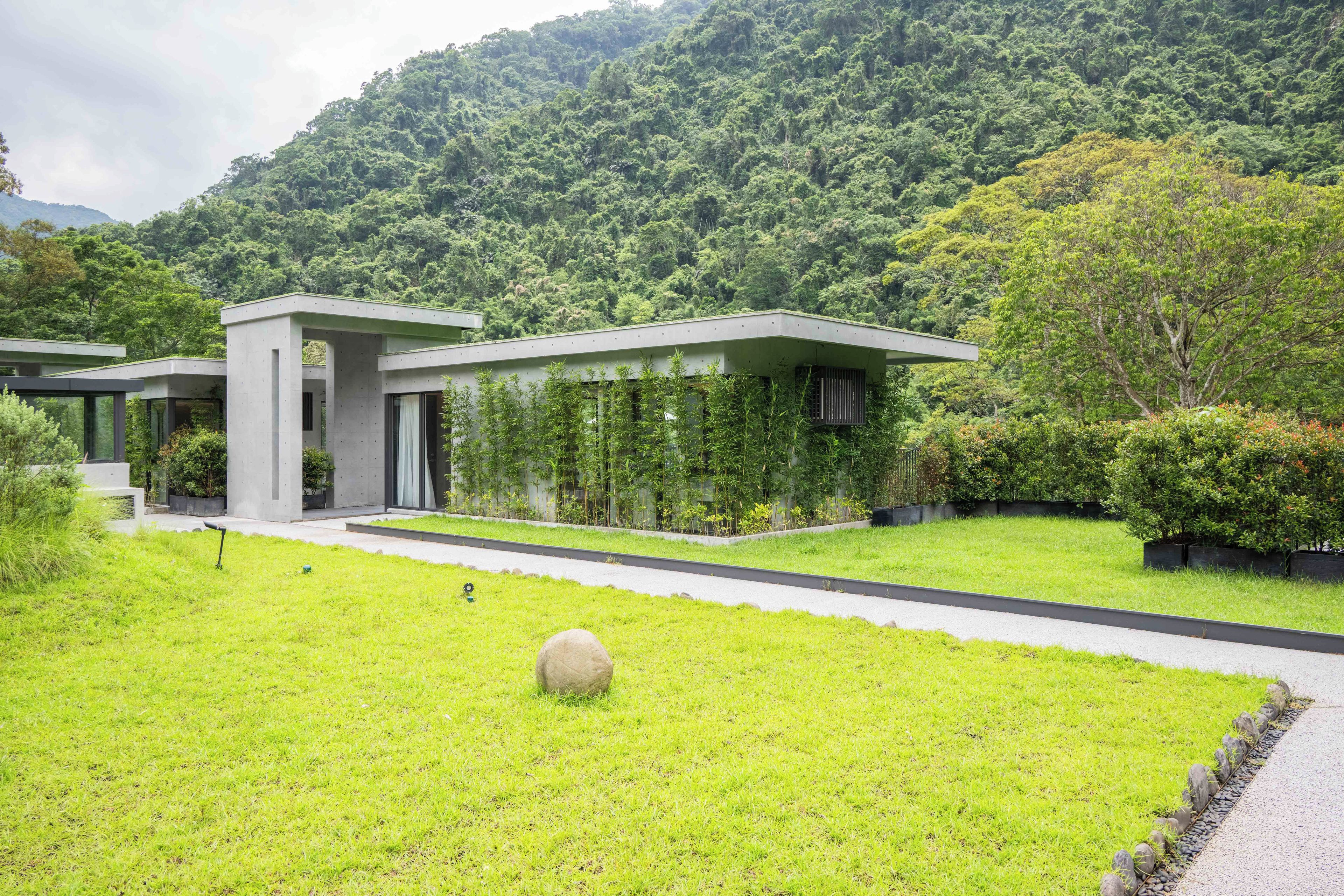 A modern building with a flat roof, surrounded by lush greenery and a well-maintained lawn.