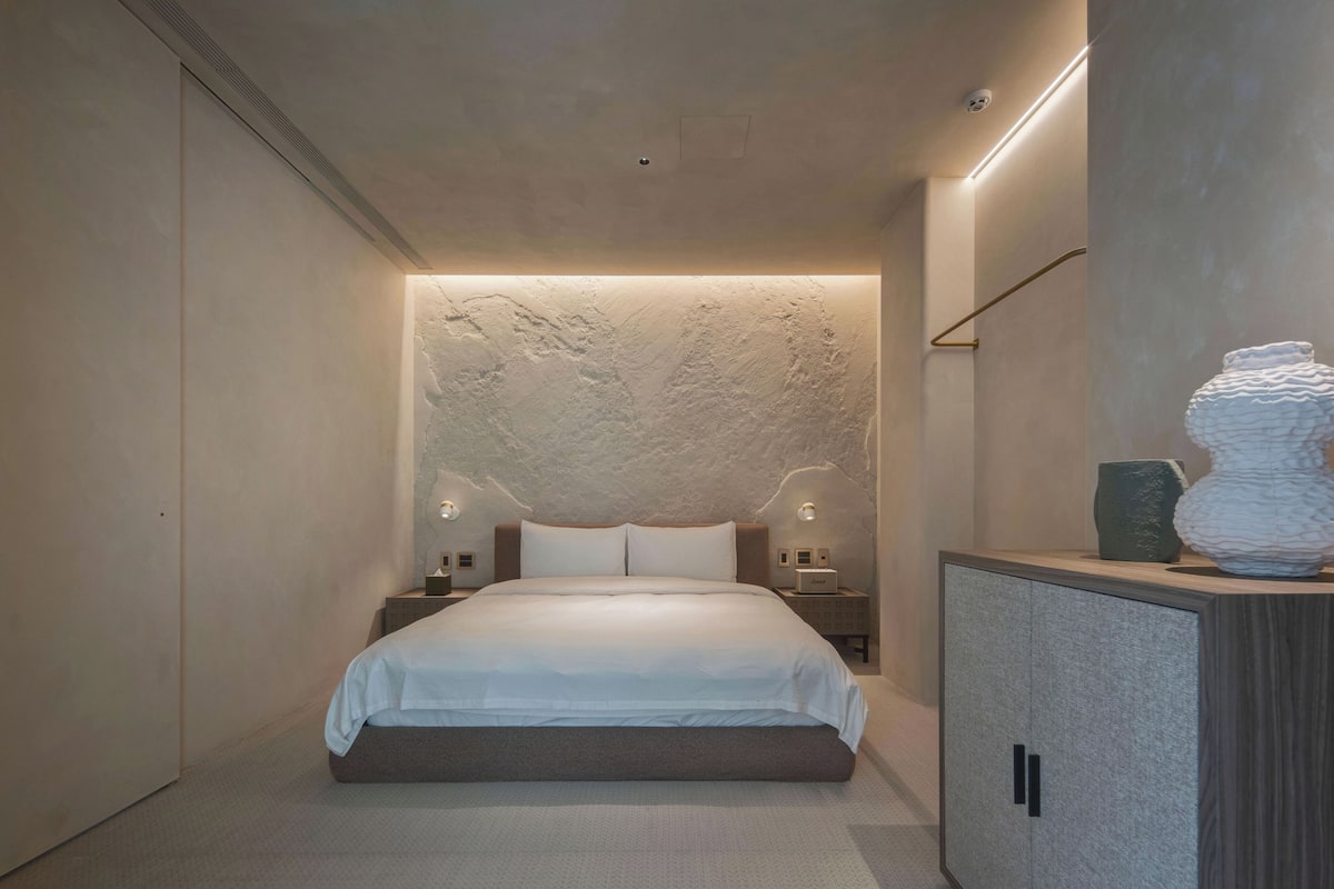 Een moderne slaapkamer met een groot bed, nachtkastjes, een kast en een gestructureerde muur.