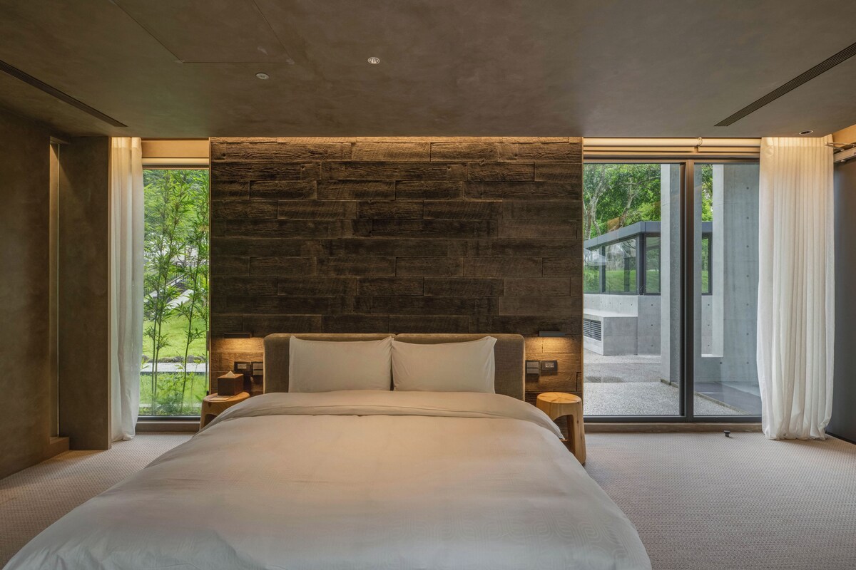 Een moderne slaapkamer met een groot bed, stenen muur en grote ramen.