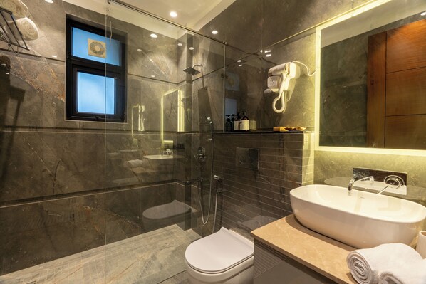 A modern bathroom with a glass-enclosed shower, a standalone toilet, and a freestanding sink. - Elivaas Gardenia 4 BHK Farmhouse  (Gurugram)