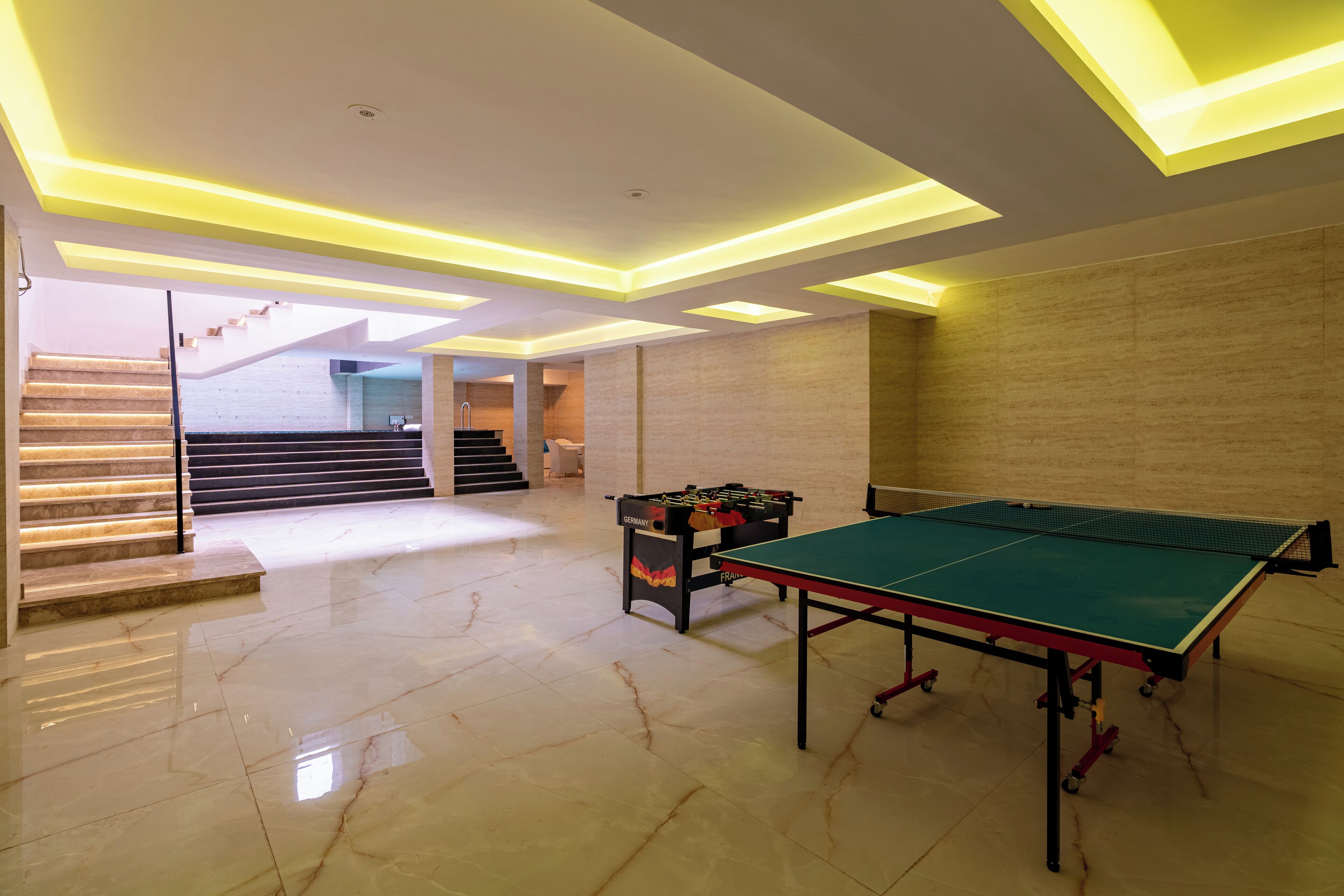 Une pièce spacieuse équipée d’une table de ping-pong, d’un baby-foot et d’un escalier menant à un niveau supérieur.