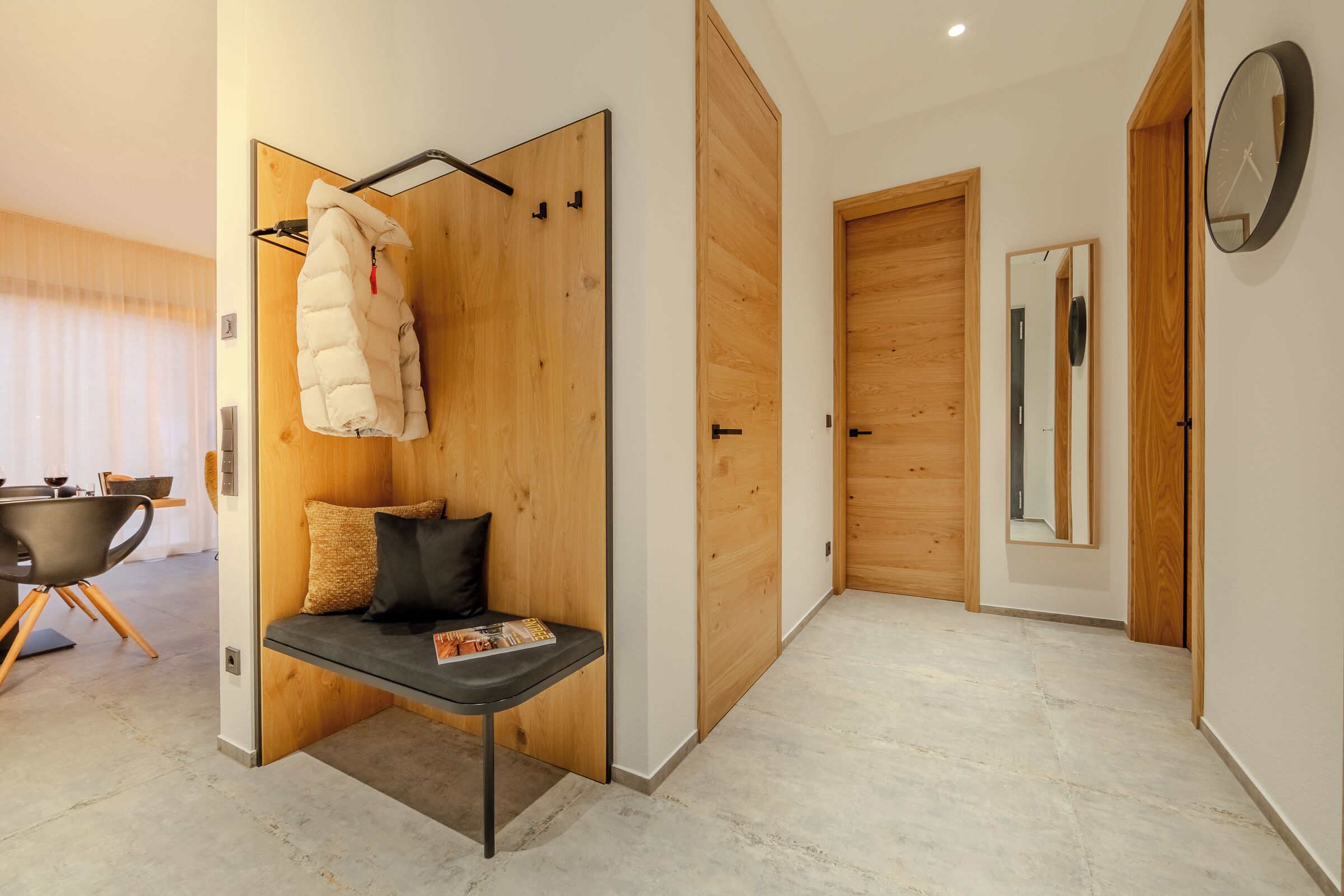 A modern hotel room with a wooden door, a bench with cushions, a coat rack, and a magazine on the bench.