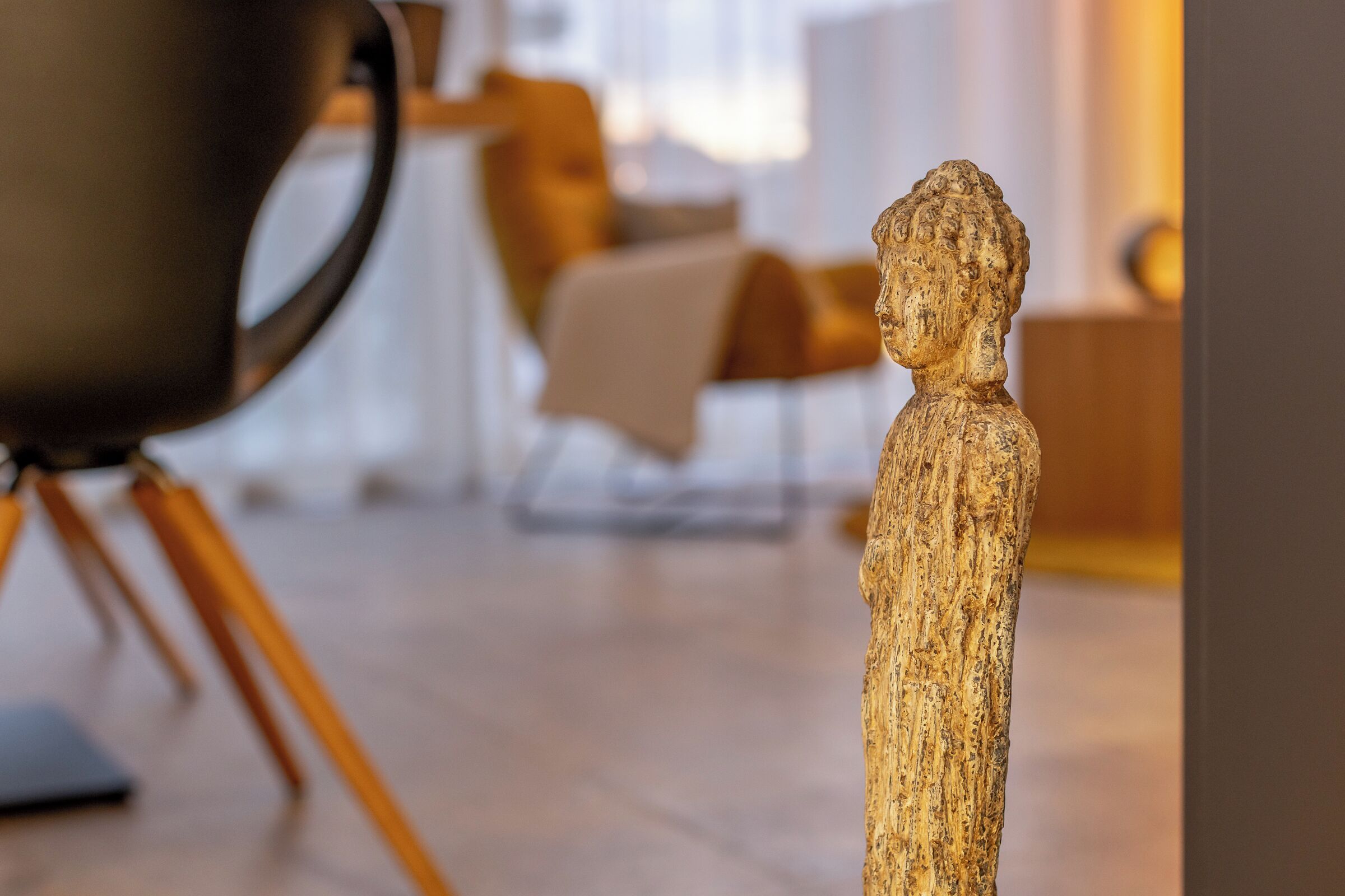 Une sculpture représentant une figure humaine, placée dans un intérieur moderne, avec un arrière-plan flou.