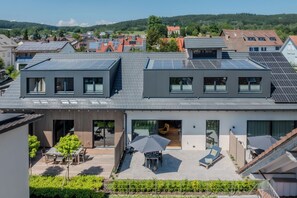 Un edificio residencial moderno con paneles solares, un patio con mobiliario exterior y una gran puerta de vidrio de entrada.