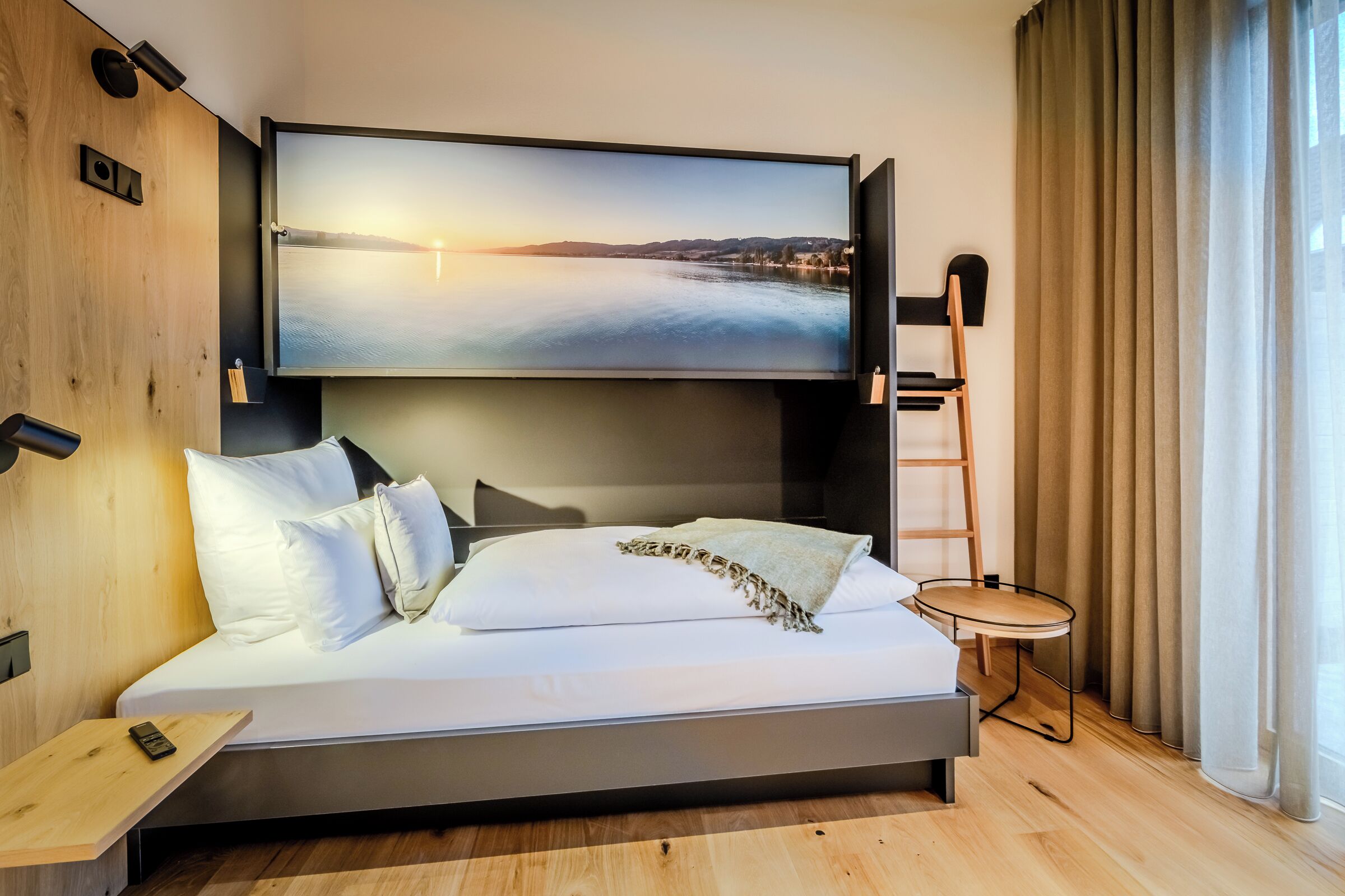 Ein modernes Hotelzimmer mit einem großen Bett, einem Wand-Fernseher, einem kleinen Tisch und einem Sessel.