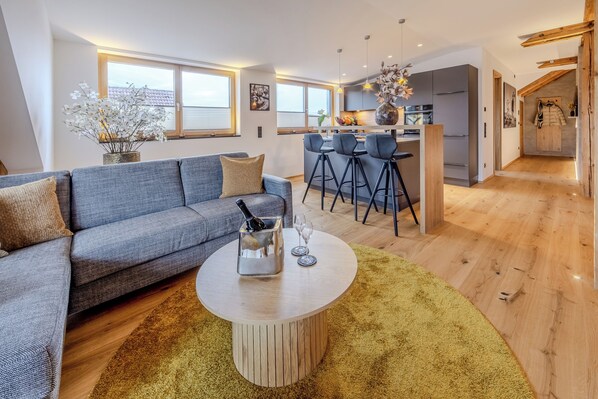 A modern living room with a grey sofa, a round coffee table, and a kitchen area with a bar and stools. - Feuerwache am See (Öhningen)