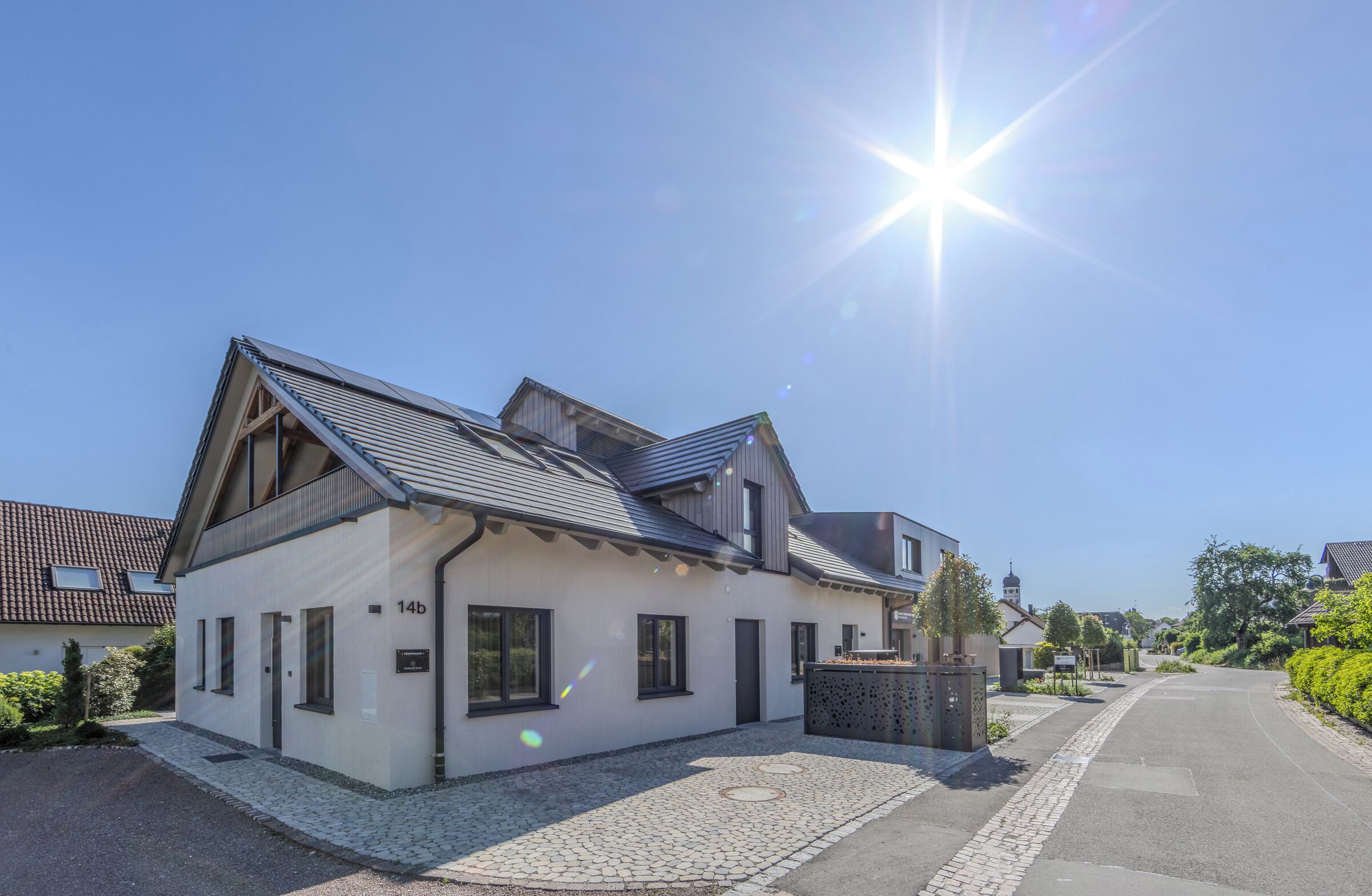 Ein modernes, zweistöckiges Haus mit geneigtem Dach, einer Auffahrt und einem kleinen Garten.