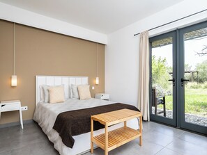 Ein modernes Schlafzimmer mit einem großen Bett, Nachttischen, einem Holztischchen und einer Schiebeglastür, die auf einen Balkon führt.