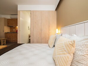 Quarto com uma cama grande, guarda-roupa de madeira e uma pequena cozinha no fundo.
