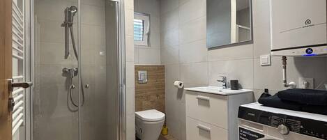 Un baño moderno con ducha de vidrio, inodoro, lavamanos y lavadora.