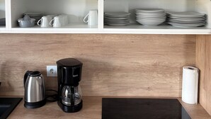 A kitchen with white shelves, a coffee maker, a kettle, and a black induction cooktop.