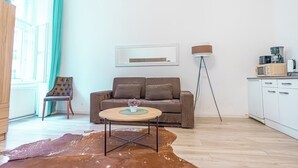 Een moderne woonkamer met een bank, een salontafel, een stoel, een vloerlamp en een keuken met inbouwapparatuur.
