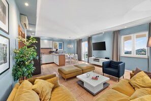 A modern living room with a sofa, ottoman, and a coffee table. There is a TV, a plant, and a view of the outside. - MOLUNAT DUBROVNIK (Gornji Brgat)