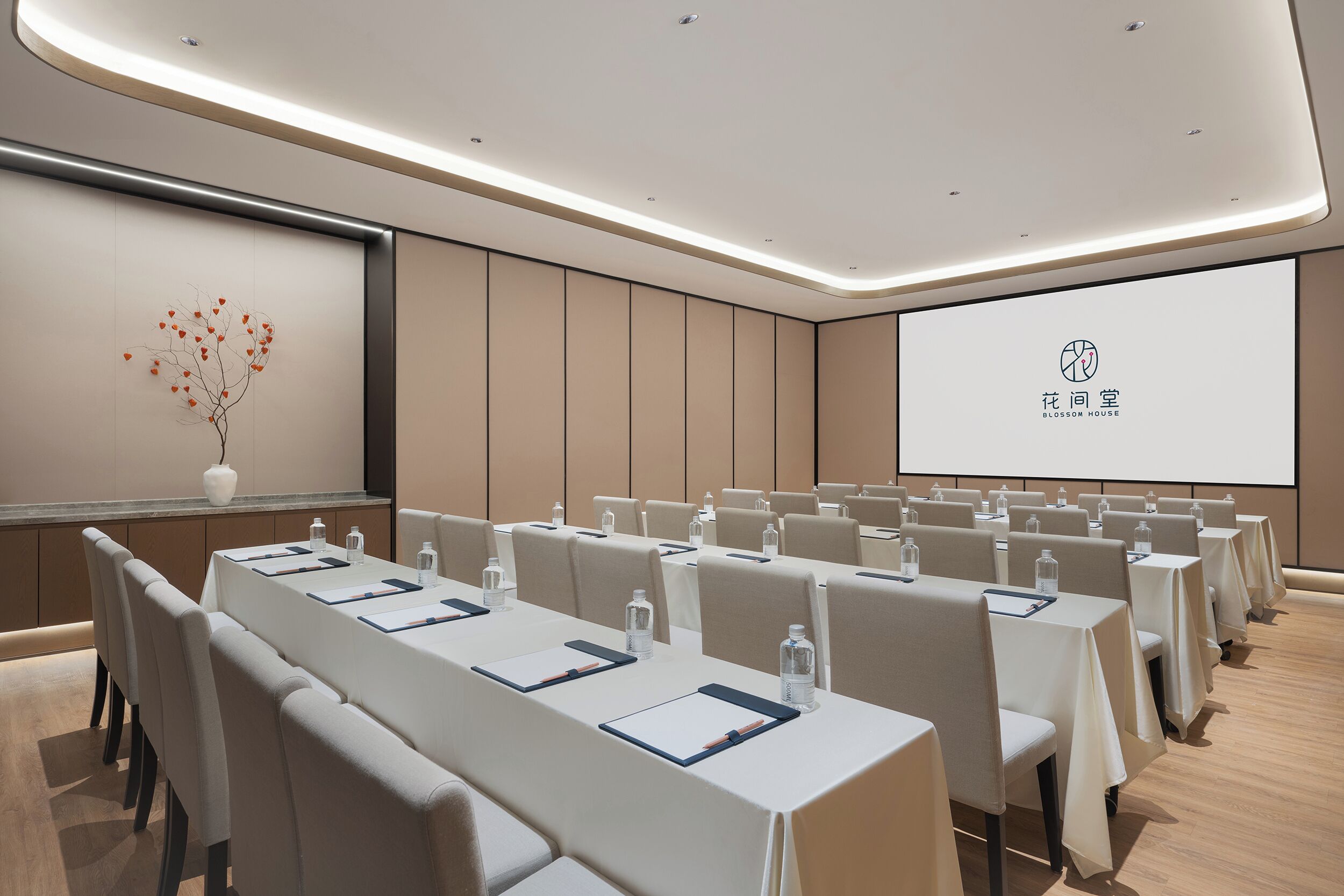 A conference room with rows of tables, chairs, and a projector screen displaying a logo.