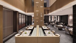 Eine moderne Hotelhalle mit einer zentralen Sitzgruppe, mehreren Esstischen und einer hohen Decke mit freiliegenden Balken.