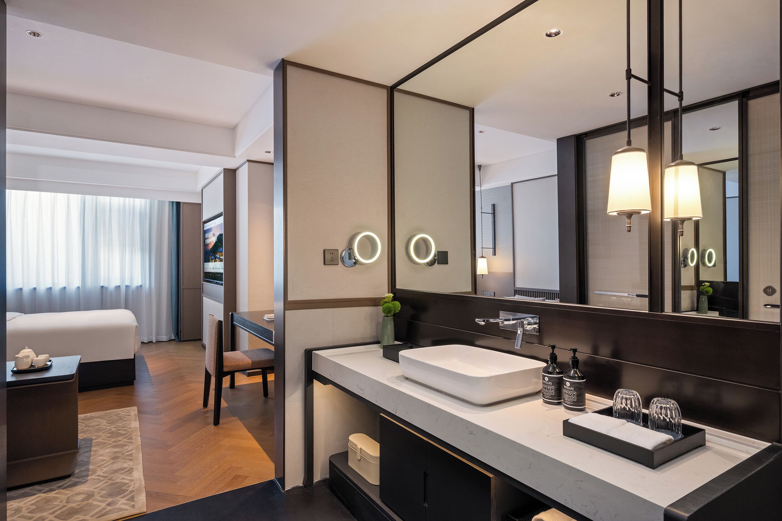 A modern hotel bathroom with a large mirror, a white sink, and a vanity with a black countertop.