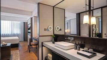 A modern hotel bathroom with a large mirror, a white sink, and a vanity with a black countertop.