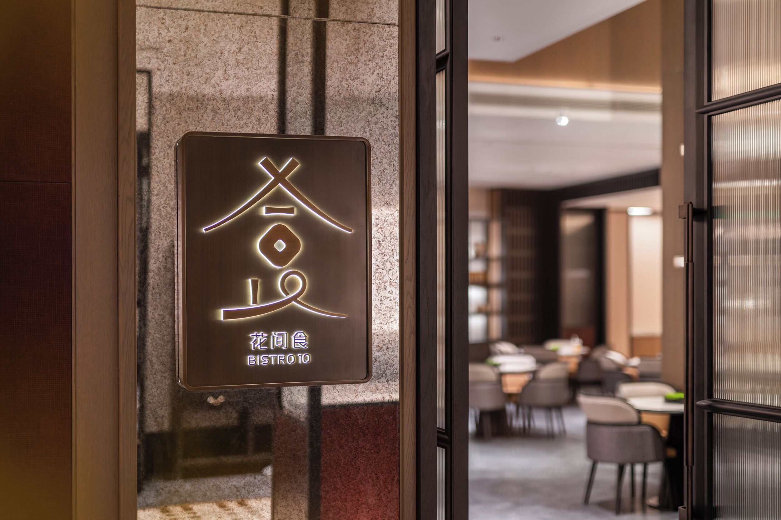 Un letrero con caracteres chinos iluminados y el nombre 'Bistro 10' en un ambiente interior moderno.
