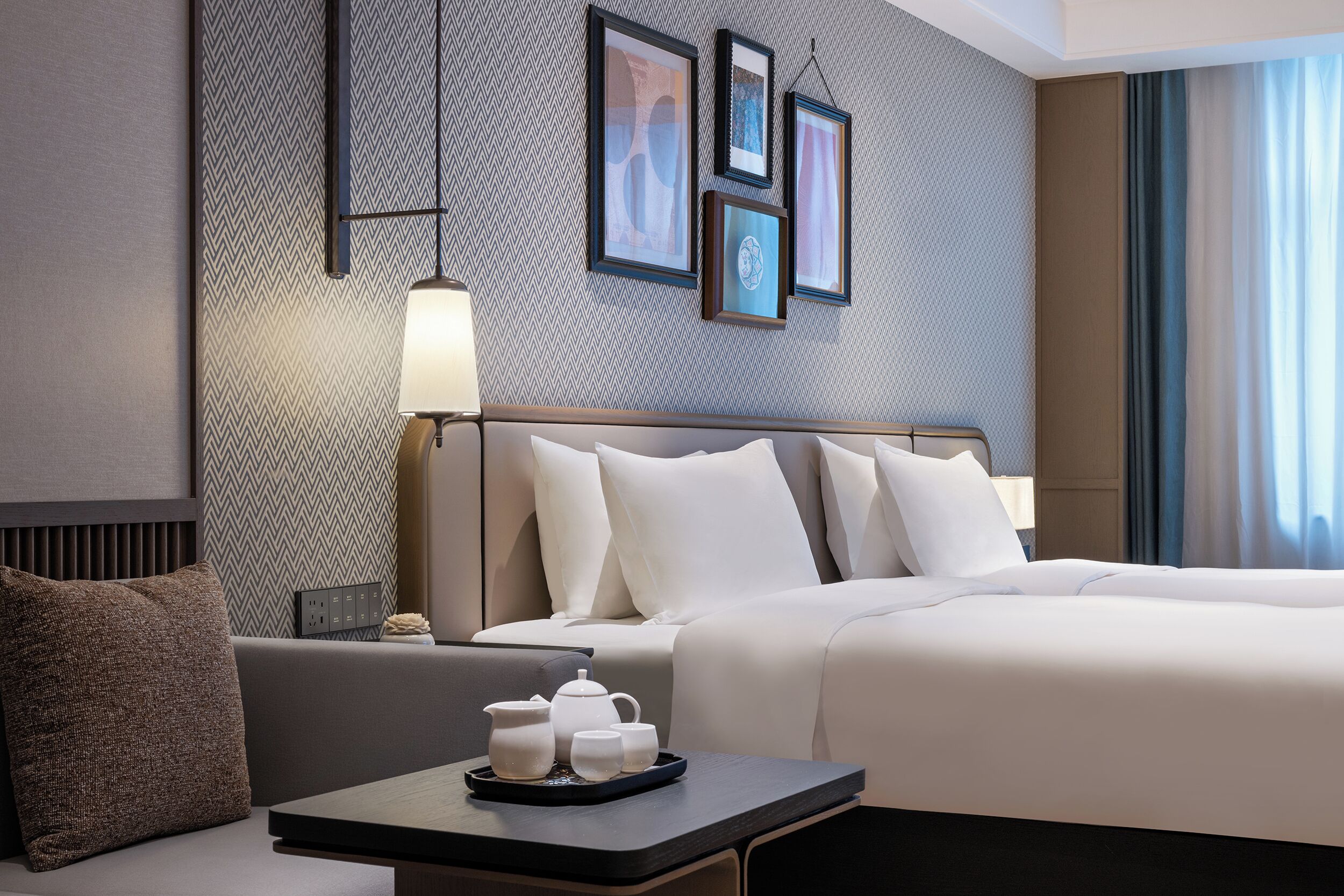 A modern hotel room with a large bed, a bedside table with a lamp, and framed artwork on the wall.
