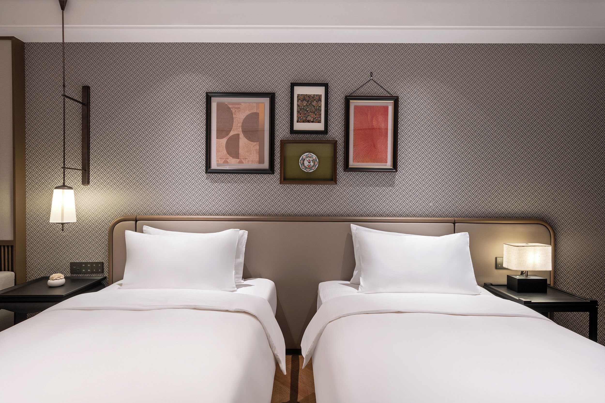Habitación de hotel con dos camas, un cabecero, una pared con papel tapiz estampado y tres obras de arte enmarcadas.