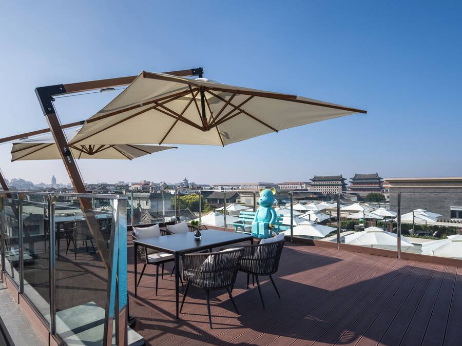 Eine Dachterrasse mit Tisch und Stühlen, einem großen Sonnenschirm und Blick auf eine Stadtlandschaft.