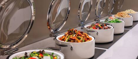 Una barra de buffet con diversos platos en ollas blancas, cada una con tapa metálica.