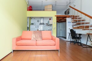 A living room with a sofa, a desk with a chair, a staircase, and a kitchen area. - GuestHost - Cozy 30sqm studio apartment located on the third floor of a typical Milanese ringhiera building with elevator.The property is set in a strategic area, just a few minutes walk from the “Gerusalemme” & “Domodossola” metro stops (M5 Lila (Milan)