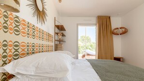 Ein Schlafzimmer mit Bett, einem Wandmuster, einem Fenster mit Vorhängen und Blick ins Freie.