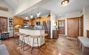 A spacious kitchen with a central island, wooden cabinets, stainless steel appliances, and pendant lighting.