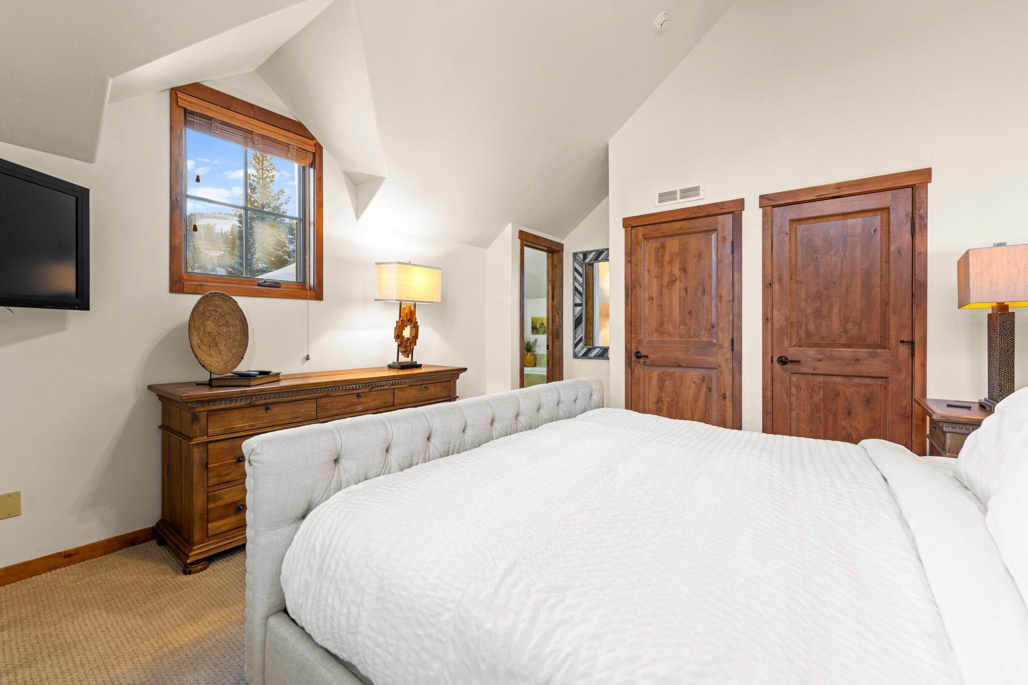 Een slaapkamer met een groot bed, een houten kledingkast en een raam met uitzicht op bomen.