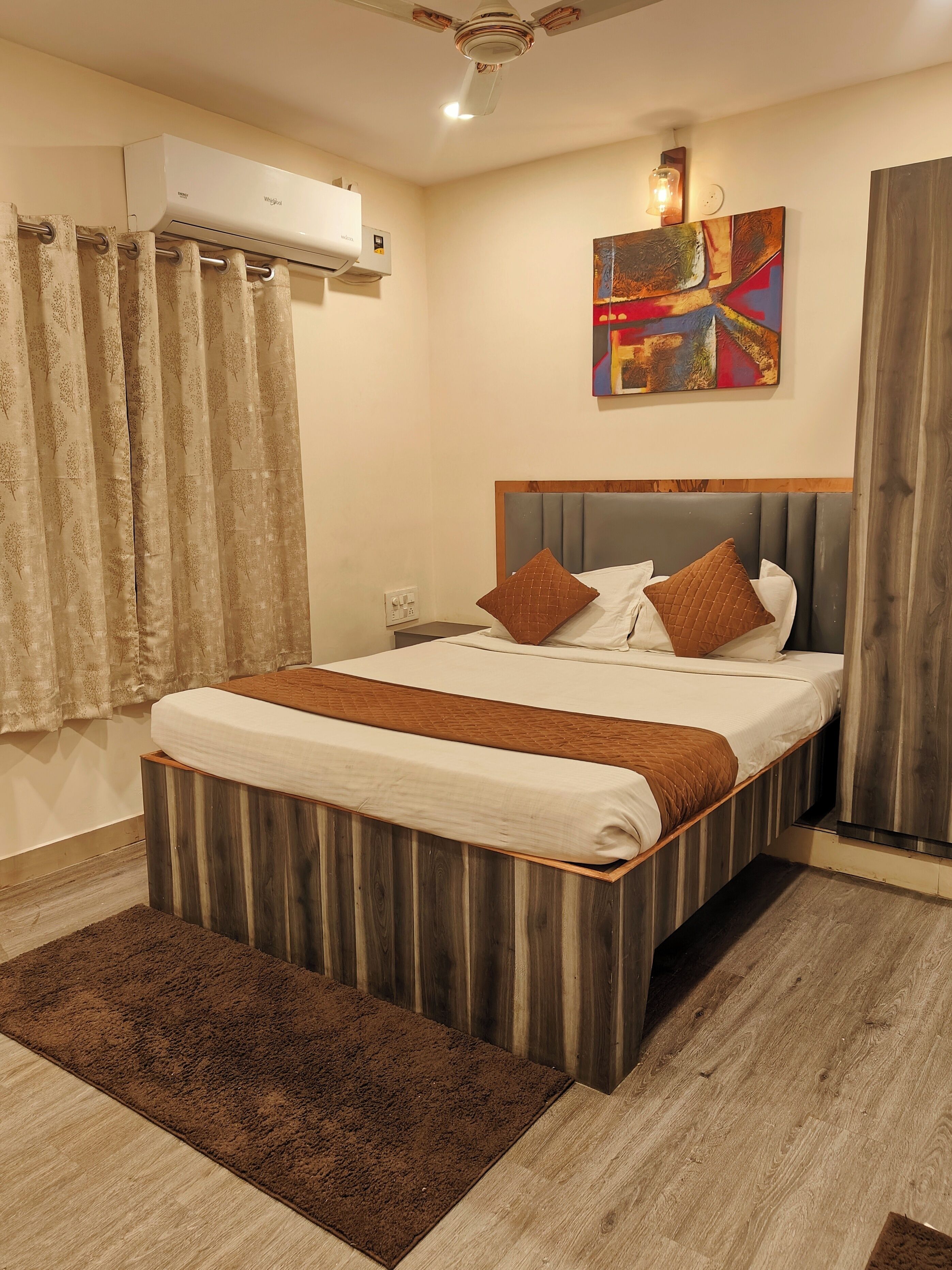A bedroom with a bed, a ceiling fan, an air conditioning unit, a painting, and a wooden headboard.