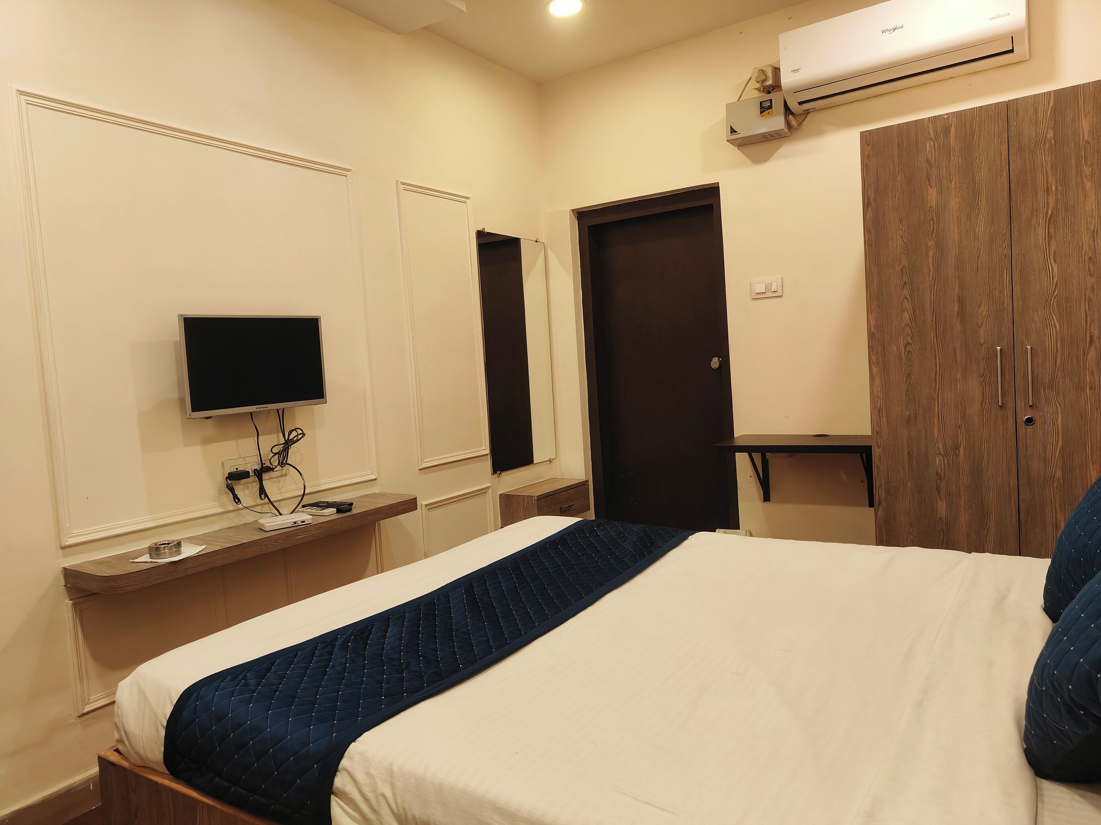 A hotel room with a bed, a television, a wardrobe, and an air conditioning unit.