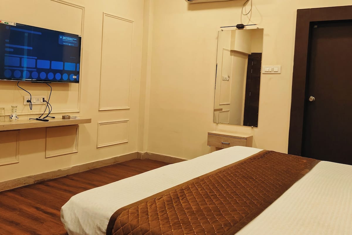Ein Hotelzimmer mit einem Bett, einem an der Wand befestigten Flachbildfernseher, einer Klimaanlage, einem Spiegel und einem Holzboden.