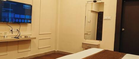 A hotel room with a bed, a flat-screen TV mounted on the wall, an air conditioning unit, a mirror, and a wooden floor.