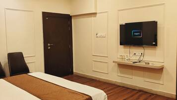 Una habitación de hotel con una cama, un televisor montado en la pared, piso de madera y ventilador de techo.