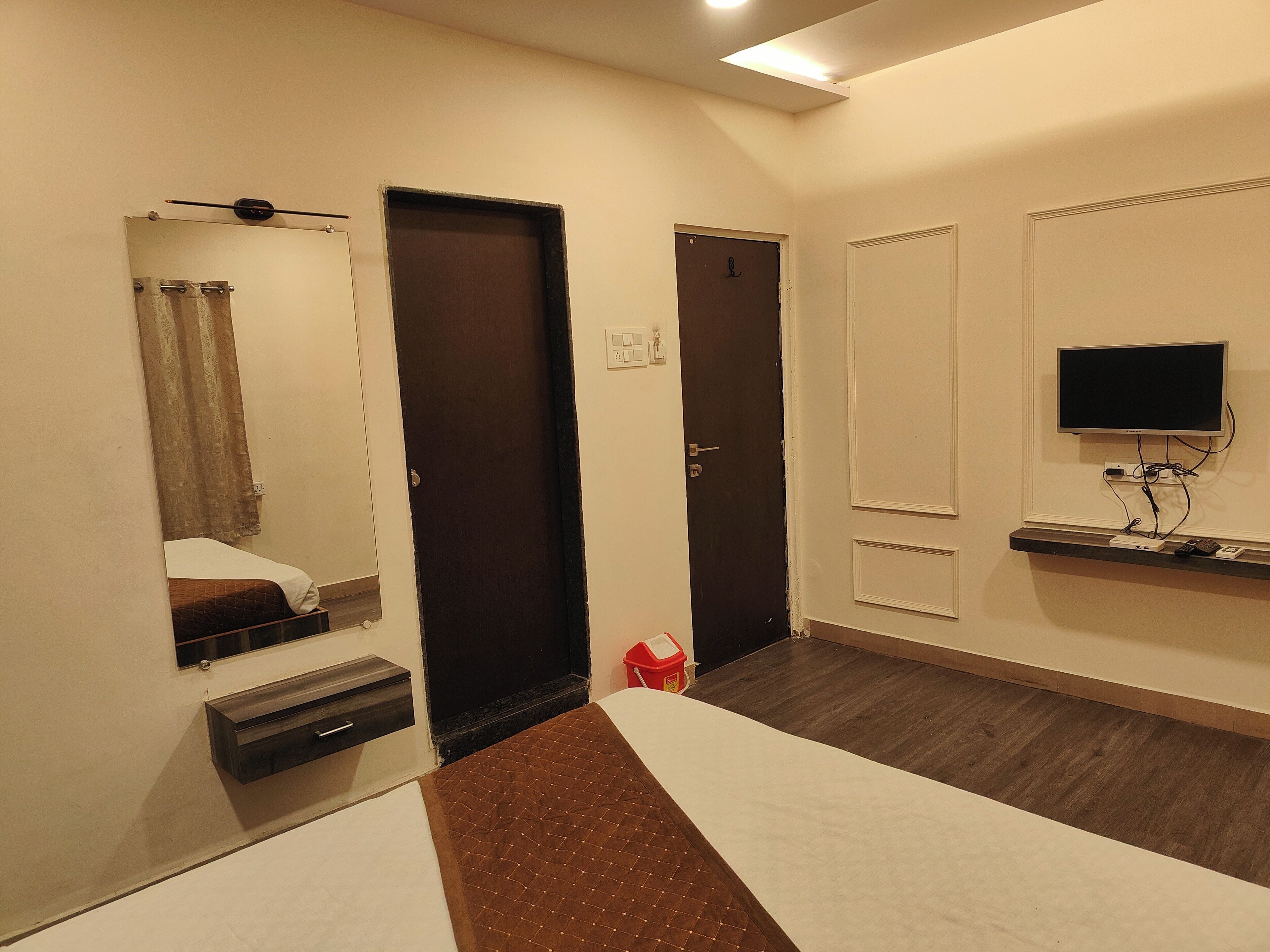 Une chambre d’hôtel comprenant un lit, un téléviseur fixé au mur, un petit bureau avec un ordinateur et une porte donnant sur une autre pièce.