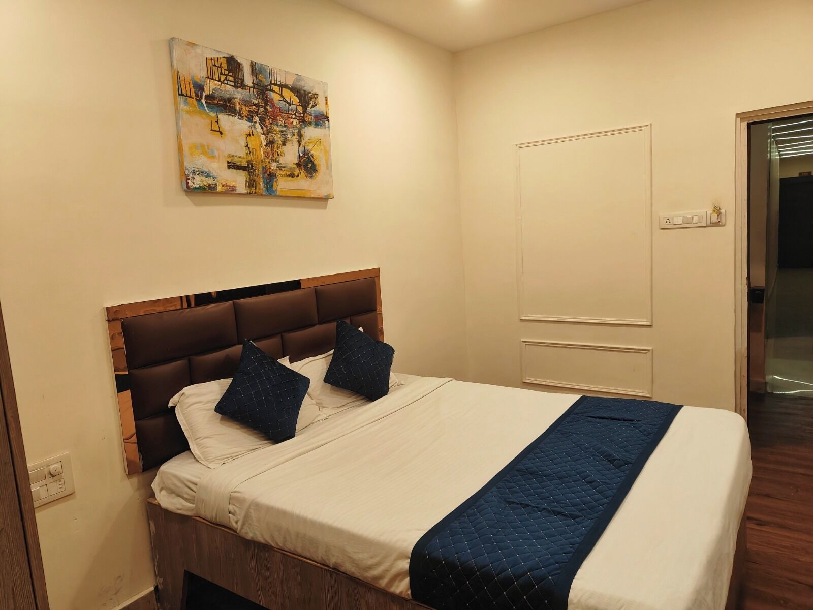 Uma cama bem arrumada com um cobertor acolchoado e duas almofadas, uma cabeceira de madeira e um quadro na parede.