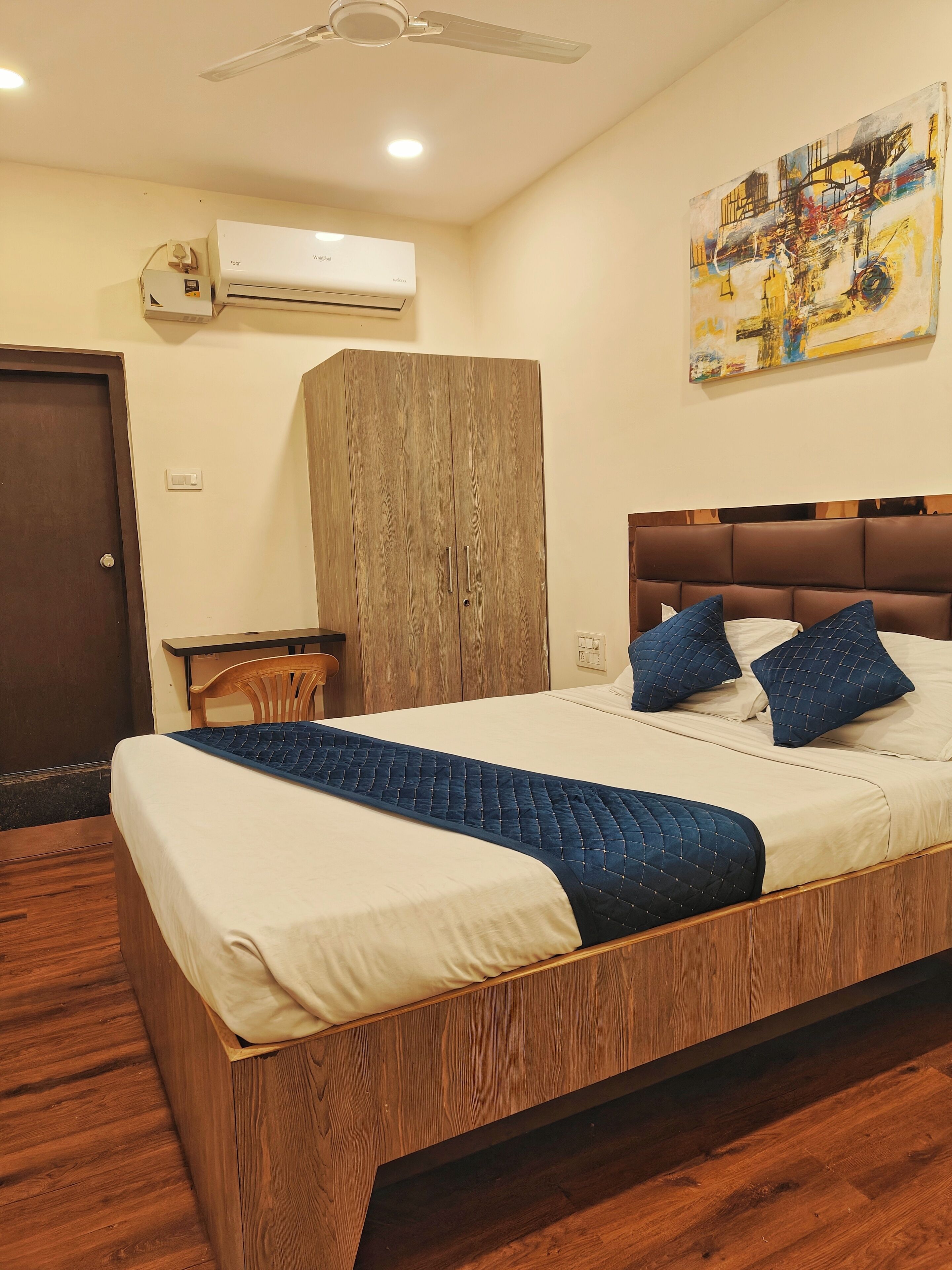 Un dormitorio ordenado con estructura de cama de madera, cabecera, mesita de noche, equipo de aire acondicionado y un cuadro en la pared.