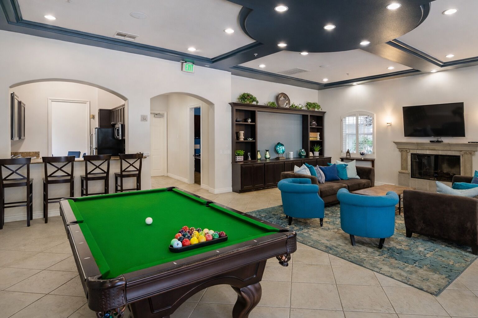 A pool table with balls, a sofa set, a TV, and a fireplace in a well-lit room with an arched doorway and a bookshelf.