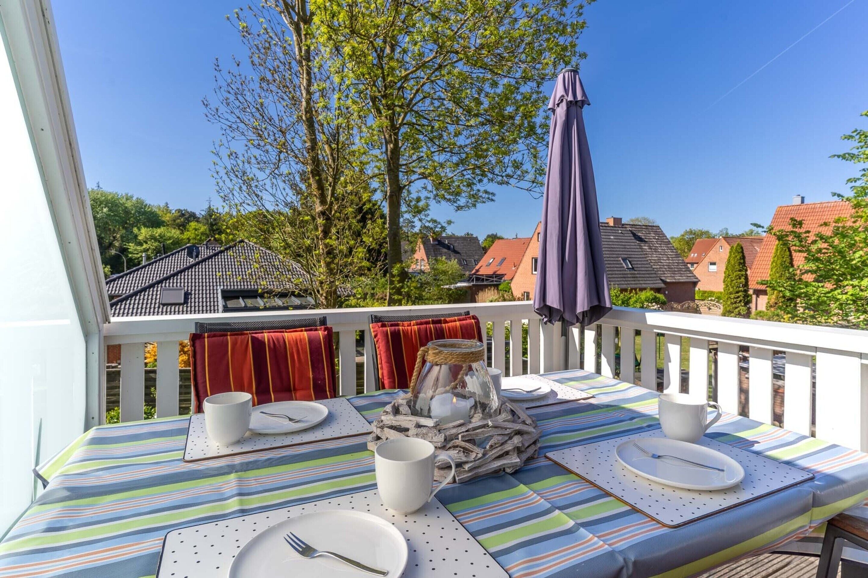 Une table à manger dressée avec des assiettes, des couverts et un chandelier, sur un balcon offrant une vue sur des maisons et des arbres.