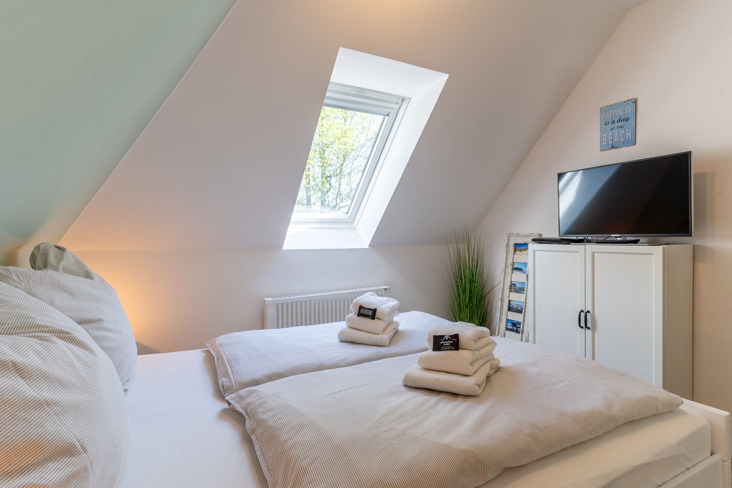 A bedroom with two beds, a TV, a cabinet with photos, and a skylight.