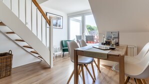 A modern dining area with a wooden table, white chairs, and a view of the outdoors through large windows. - Ferienwohnung mit Balkon in St.peter-ording (St. Peter-Ording)